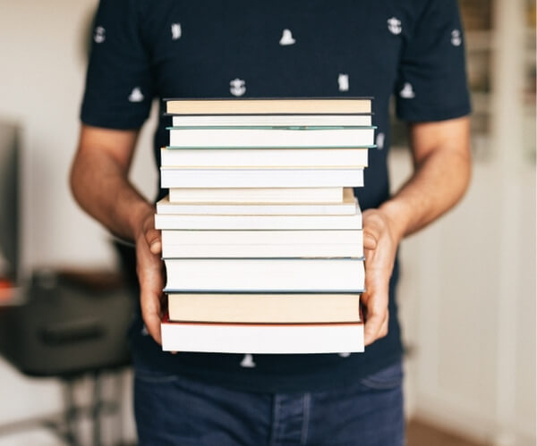 Najlepsze książki o inteligencji emocjonalnej (TOP 13). Co warto przeczytać, żeby nie stracić czasu? Na obrazku mężczyzna trzymający stos książek w swoich rękach.